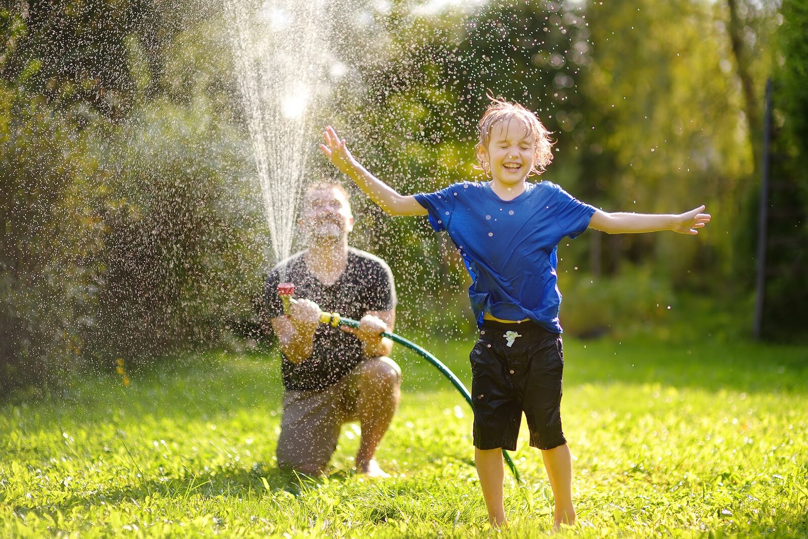 A father and son playing in the spray of a home sprinkler system